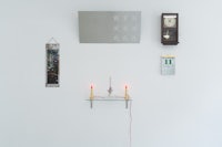 a white wall with several clocks and candles on it